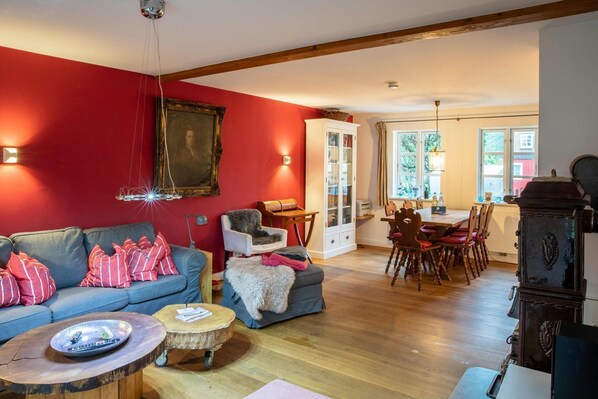 A living room with a red wall, a blue sofa, a wooden dining table with chairs, and a vintage stove.