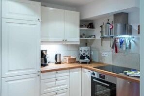 A compact kitchen with white cabinets, a coffee machine, a toaster, and a hanging rack with kitchen utensils.
