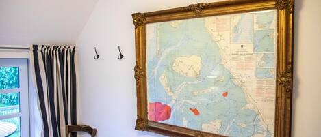 Um mapa emoldurado pendurado numa parede, uma cadeira com almofada estampada em formato de estrela, e uma janela com cortinas listradas.