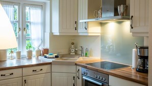 A kitchen with white cabinets, a stove, a sink, and a window with curtains.