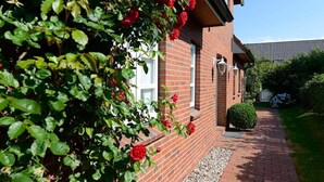 A brick building with a pathway leading to a door, surrounded by greenery and a hedge.