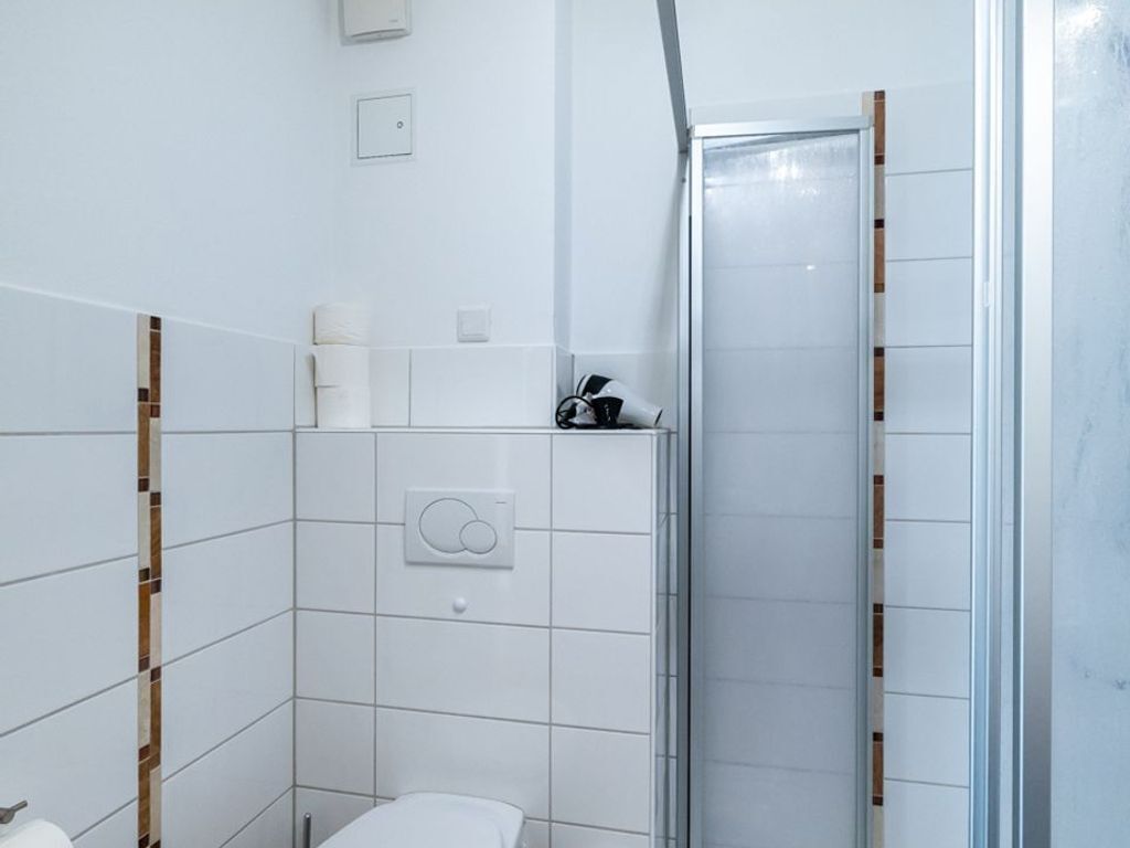 Ein Badezimmer mit weißen Fliesen, einer Toilette, einer Duschkabine mit Glastür und einem Handtuchspender.