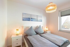 Un dormitorio con una cama, dos mesitas de noche, una lámpara colgante y una ventana con persianas.