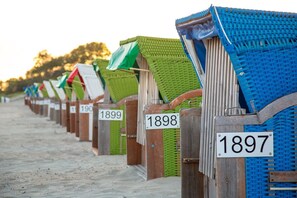 Eine Reihe von Strandhäusern mit den Nummern 1897 bis 1909, mit Sandstrand und Bäumen im Hintergrund.