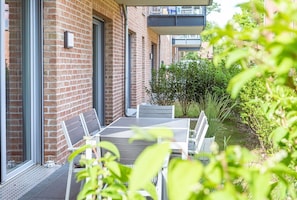 Un patio moderno al aire libre con una mesa y sillas, un muro de ladrillo y un pequeño jardín.