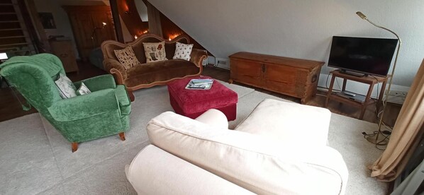 A living room with a green armchair, a brown sofa, a red ottoman, a white sofa, a wooden cabinet, and a TV on a stand.