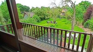 Uitzicht vanaf een balkon op een weelderige tuin met een rieten huis en een boom met paarse bladeren.