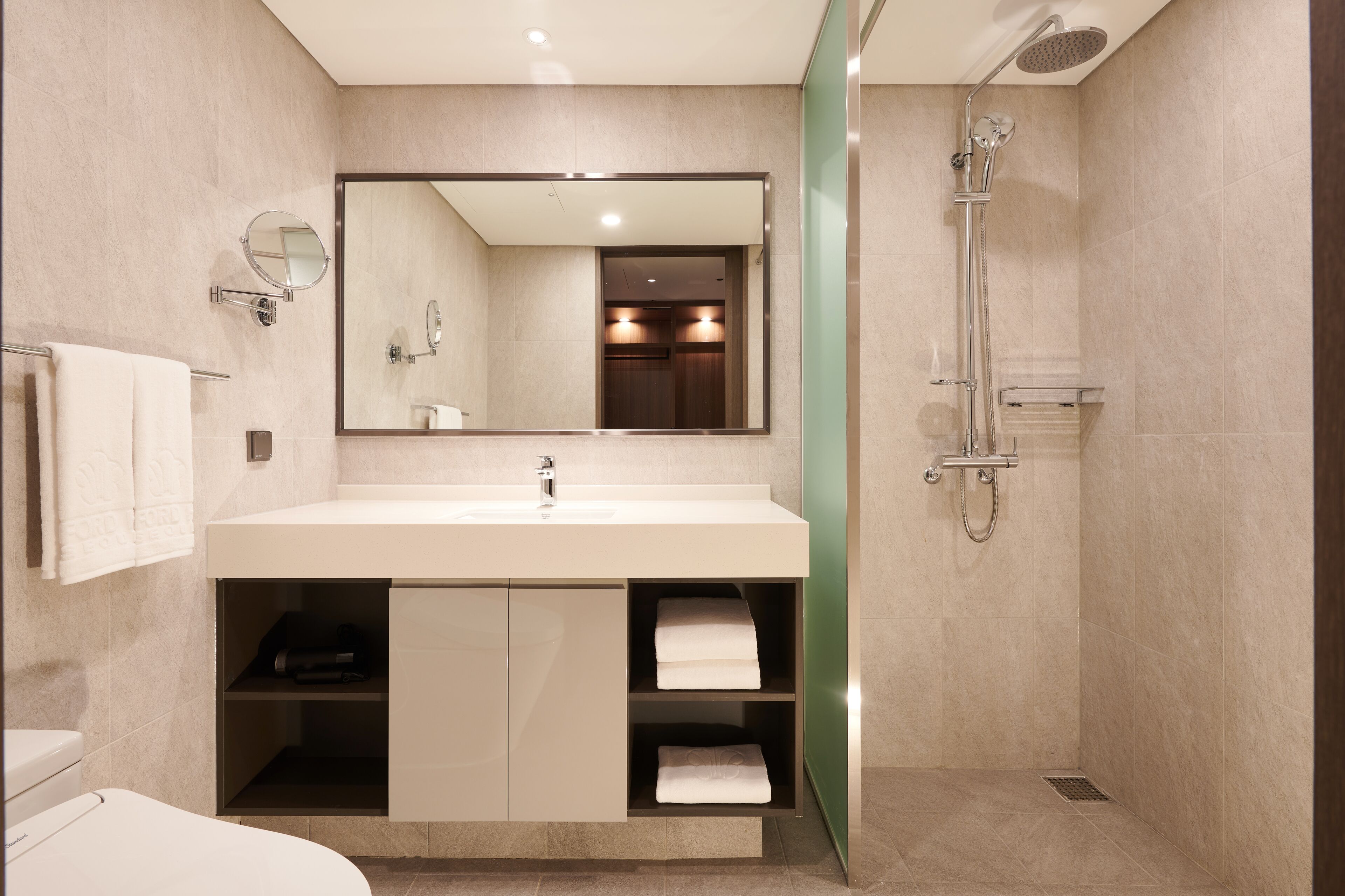 Un baño moderno con un espejo grande, un lavabo, una ducha y repisas empotradas para toallas.