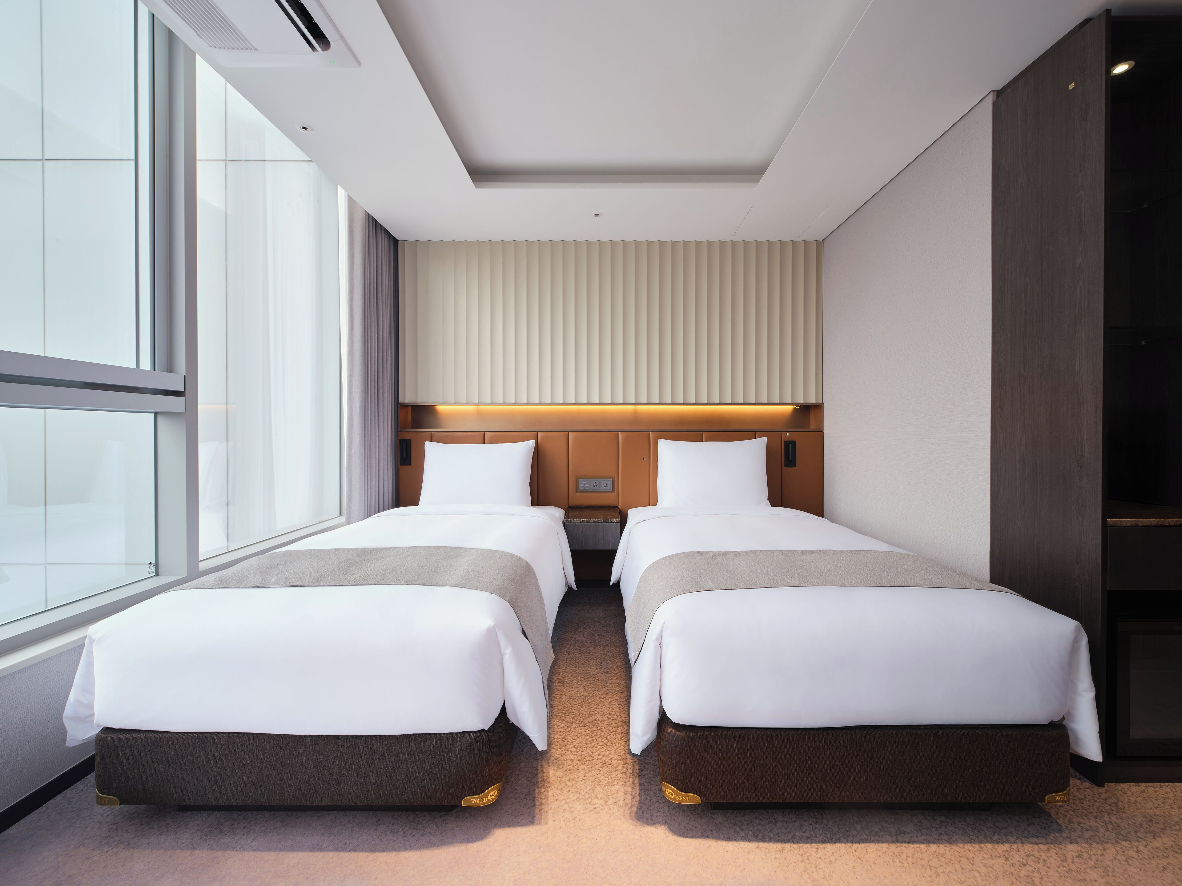 A hotel room with two beds, a large window, and a modern design.