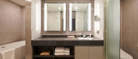 A modern bathroom with a large mirror, a bathtub, a toilet, and a vanity with shelves for towels.