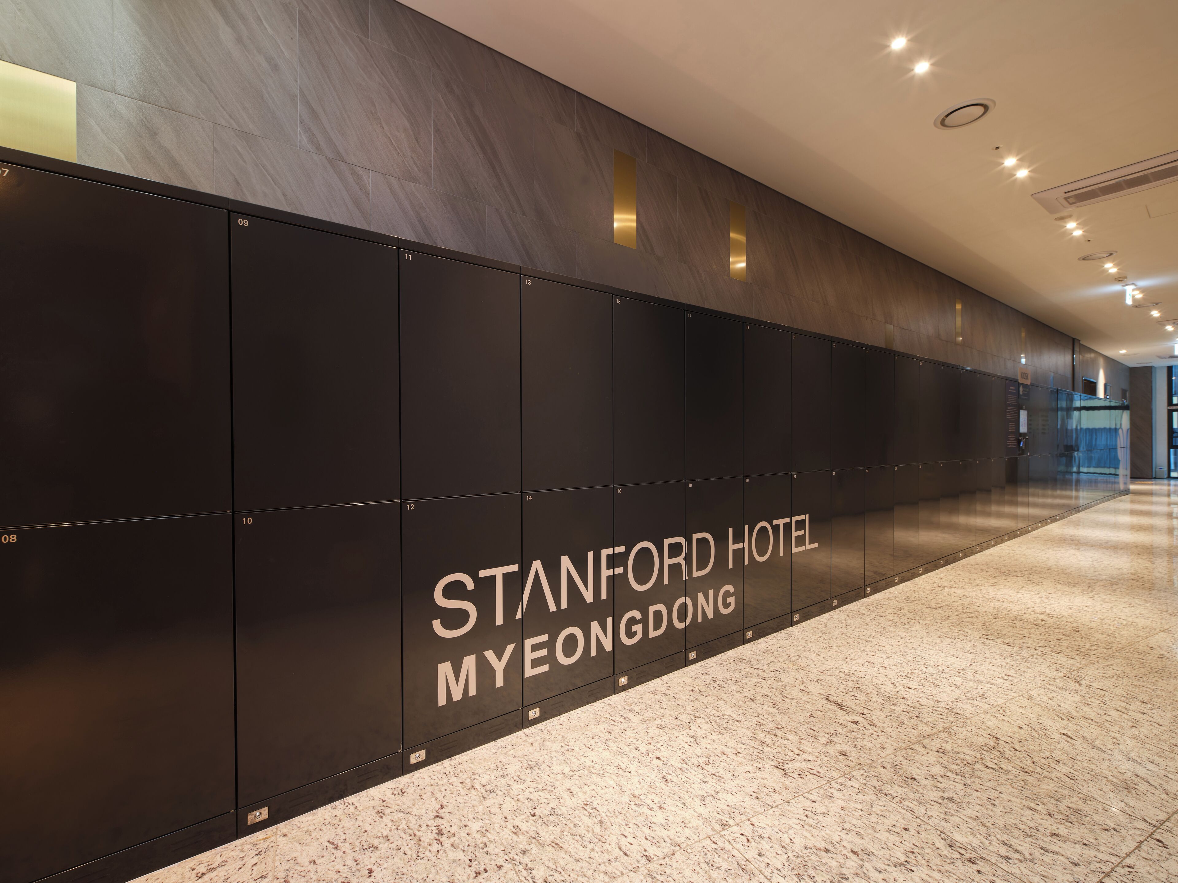 Un pasillo con taquillas y el texto "STANFORD HOTEL MYEONGDONG" en la pared.