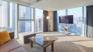 Habitación de hotel moderna con un ventanal grande, televisor de pantalla plana, sofá, mesa de centro y lámpara.