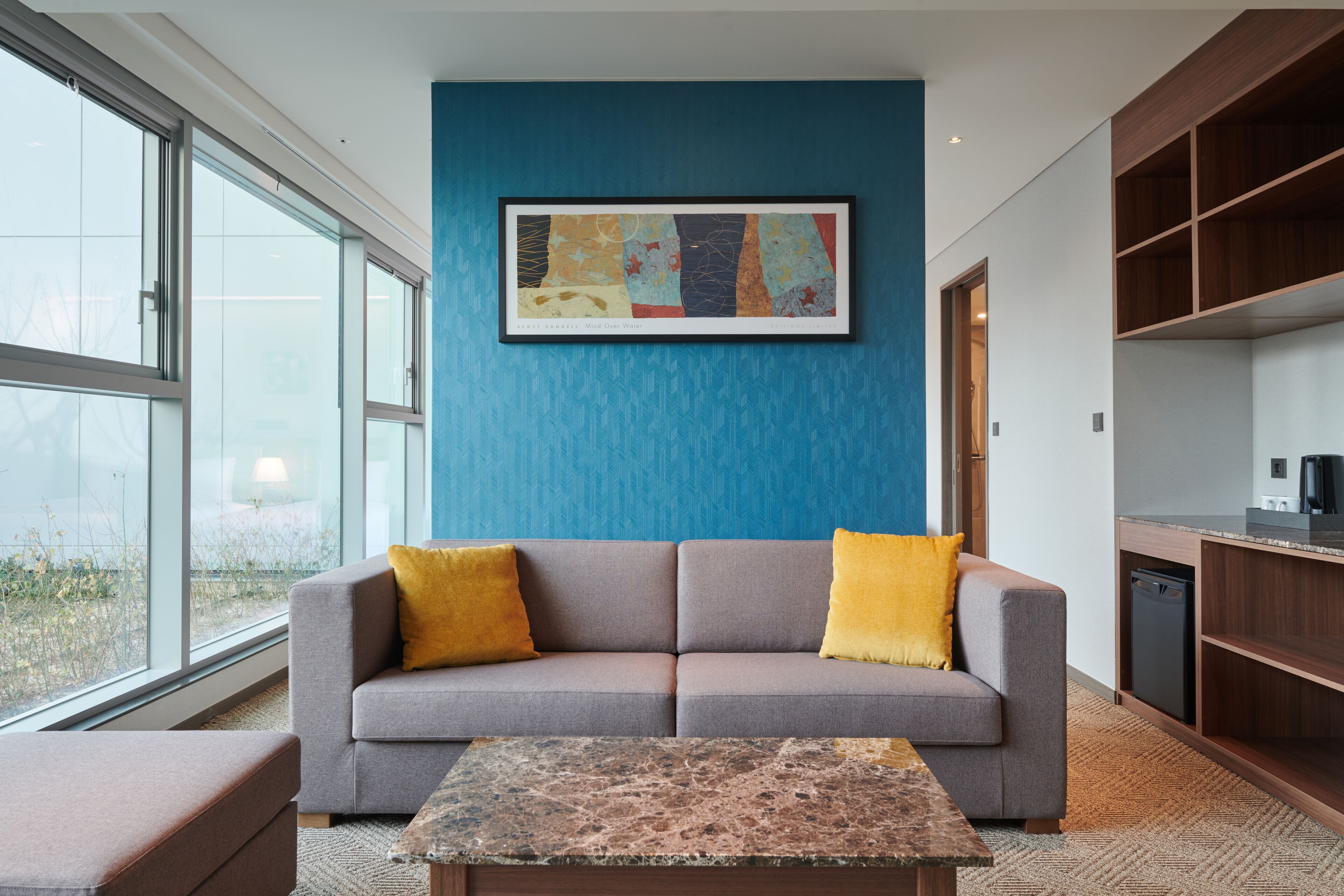 A modern living room with a grey sofa, yellow cushions, a coffee table, and a large window.