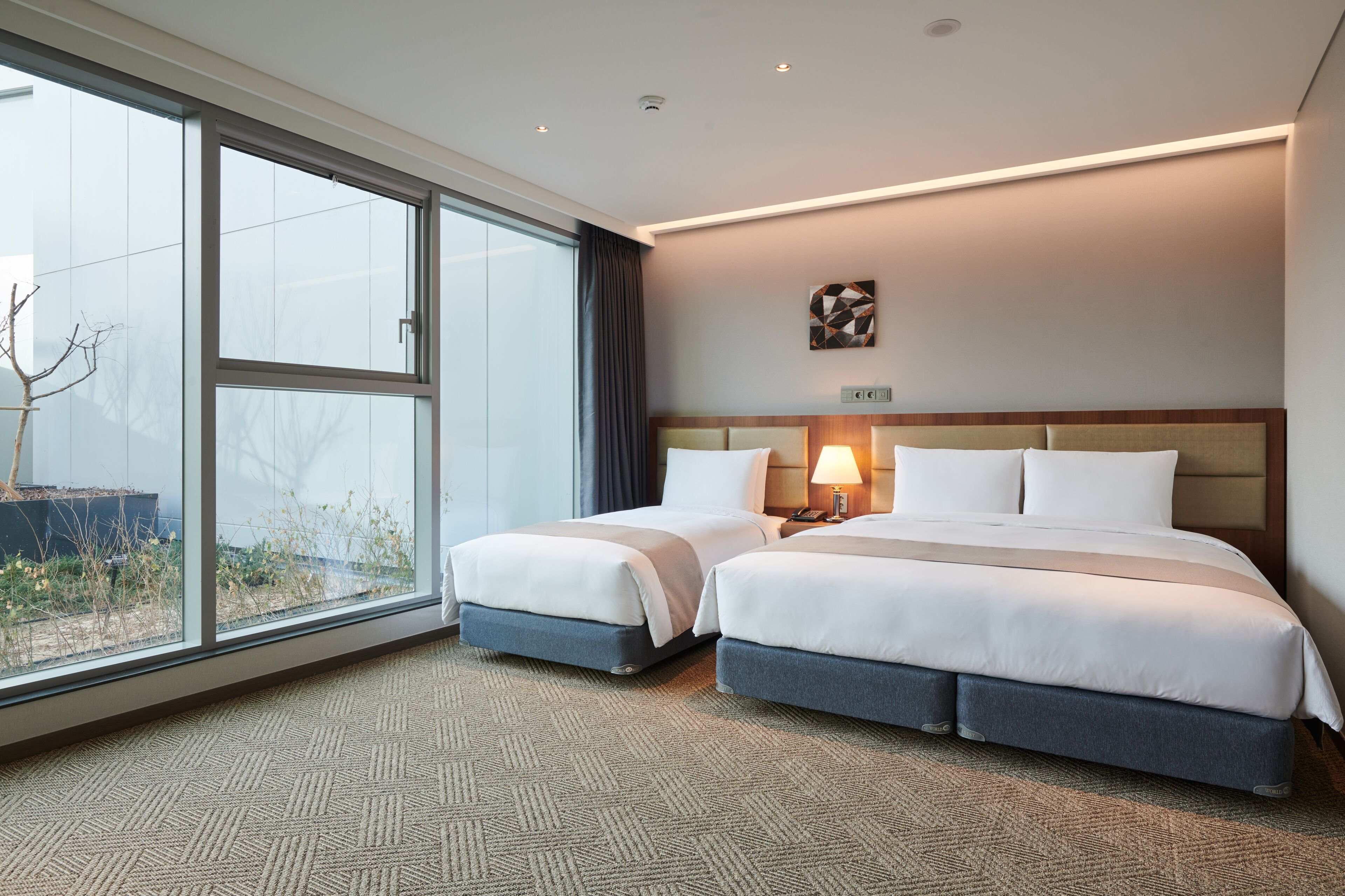 A hotel room with two beds, large windows, a view of the outdoors, and a modern design.