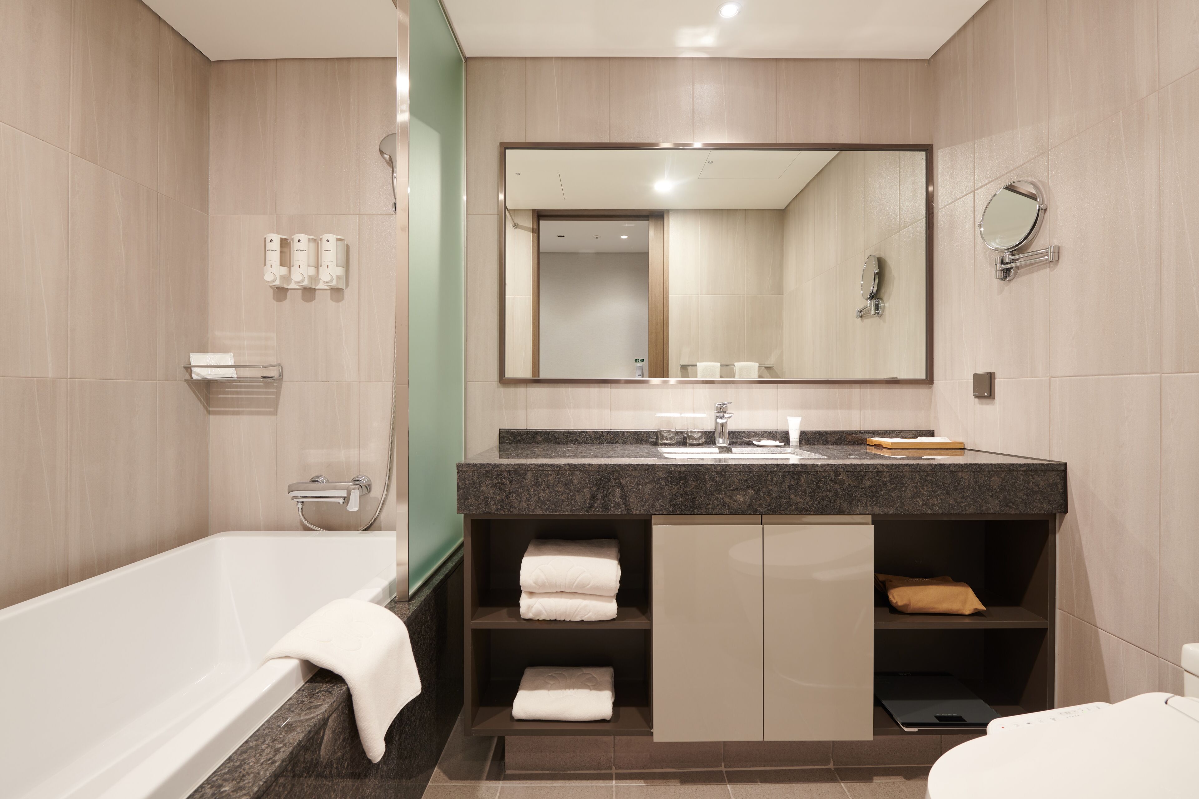 A modern bathroom with a bathtub, a large mirror, a sink, and built-in shelves with towels.