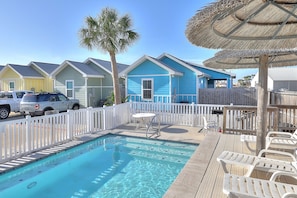 A pool area with a clear blue pool, white lounge chairs, and a wooden deck.