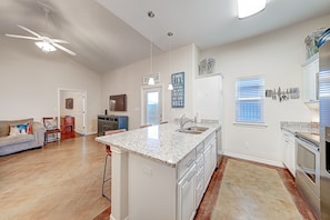 A spacious kitchen with a central island, white cabinetry, and a large window with blinds.