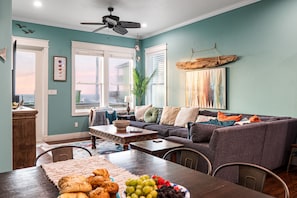 A cozy living room with a gray sofa, wooden coffee table, and a dining area with a table set for a meal. - New! Beachfront*Spectacular Views*4 bdrm House*Sleeps 14 (Crystal Beach)