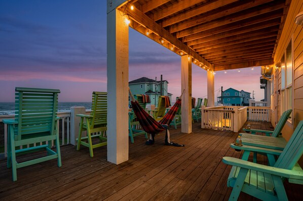 A wooden deck with chairs and a hammock, overlooking the ocean.