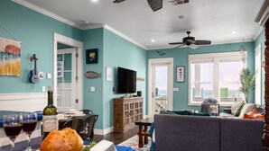 A living room with teal walls, a gray sofa, a wooden cabinet, and a dining area with a table and chairs. - New! Beachfront*Spectacular Views*4 bdrm House*Sleeps 14 (Crystal Beach)