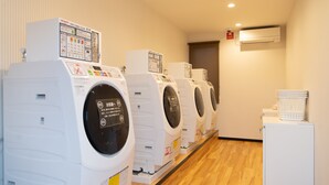 A row of white, wall-mounted laundry machines in a room with wooden flooring and a white wall. - HOTEL R9 The Yard Oyamayokokura (Oyama)
