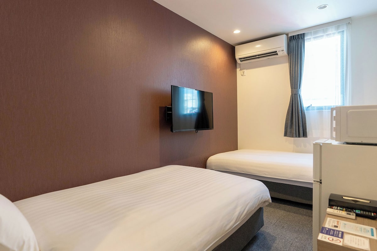 Een hotelkamer met twee bedden, een flatscreen televisie aan de muur, een airconditioning, een magnetron en een raam met gordijnen.