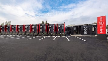 Ein Hotel mit einer Reihe schwarzer Behälter mit roten Akzenten, einem Parkplatz und einem roten Schild mit dem Namen des Hotels.