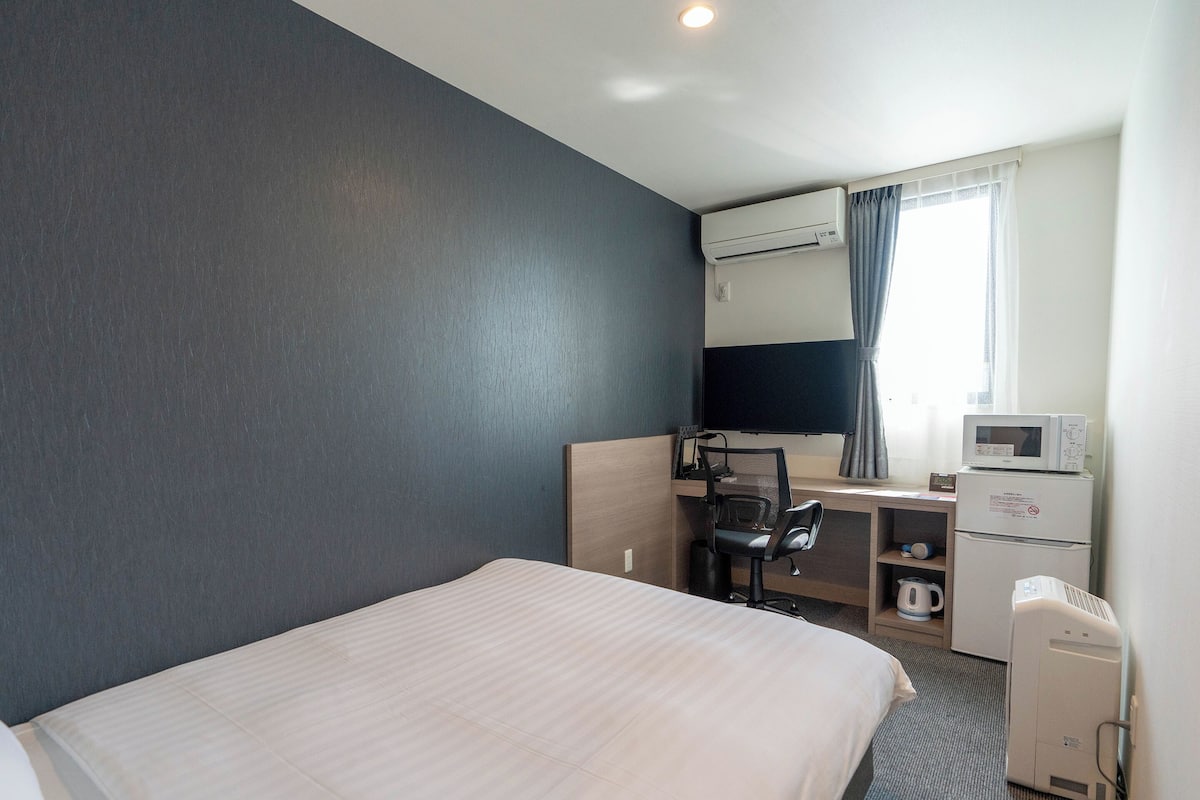 Een hotelkamer met een bed, een bureau met stoel, een magnetron, een koffiezetapparaat en een televisie.