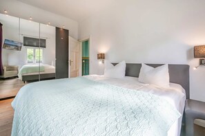 Ein modernes Schlafzimmer mit einem großen Bett, einer Couch, einem Spiegel und einer Tür zu einem weiteren Raum.