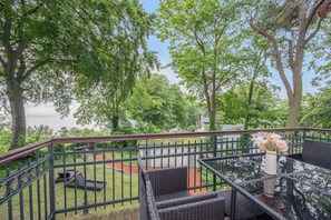 Ein Balkon mit Korbmöbeln, einem Geländer und Blick auf Bäume sowie ein Gewässer.
