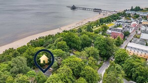 An aerial view of a coastal town with a beach, a pier, and a dense green area with a marked location.