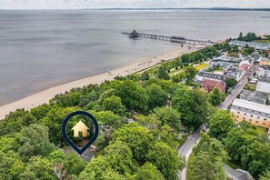 Vista aérea de un pueblo costero con playa, muelle y una zona verde densa con un lugar señalado.