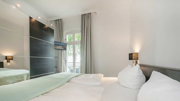 A modern hotel room with a large bed, a dark accent wall, and a view of the outdoors.