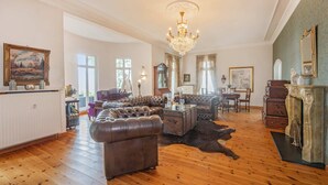A spacious living room with a large leather sofa, a chandelier, and a fireplace.