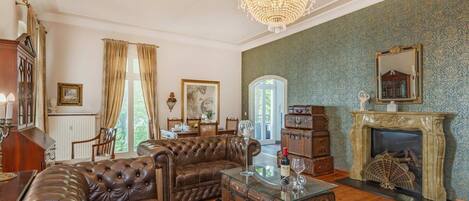 A living room with a leather sofa, a glass coffee table, a chandelier, a fireplace, and a view of the outdoors.