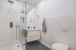 Ein modernes Badezimmer mit Duschkabine aus Glas, einem weißen Waschbecken, einem Spiegel und einer Toilette.