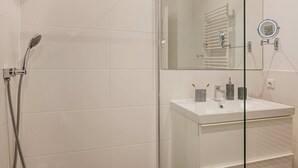 A modern bathroom with a glass shower enclosure, a white sink with a mirror, and a towel rack. - Beautiful vacation apartment in Heringsdorf with garden, only 150 m to the sea - Villa (Heringsdorf)