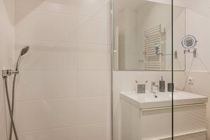 A modern bathroom with a glass shower enclosure, a white sink with a mirror, and a towel rack. - Beautiful vacation apartment in Heringsdorf with garden, only 150 m to the sea - Villa (Heringsdorf)