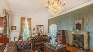 A living room with a leather sofa, a glass coffee table, a chandelier, a fireplace, and a view of the outdoors. - Beautiful vacation apartment in Heringsdorf with garden, only 150 m to the sea - Villa (Heringsdorf)
