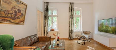 A living room with a leather sofa, a glass coffee table, a television, and a painting of horses.