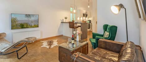 Un salon moderne avec un canapé en cuir, un fauteuil vert, une table basse en verre et un tableau accroché au mur.