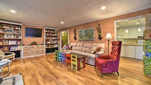 Un salon doté d’un parquet en bois, d’un canapé beige, d’un fauteuil rouge, d’un téléviseur fixé au mur et d’une bibliothèque remplie de livres et d’objets de décoration.