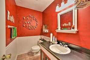 Et badeværelse med rød væg, hvid toilet og et vaskeskab med spejl.