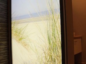 Une fenêtre donnant sur une plage et une prairie.