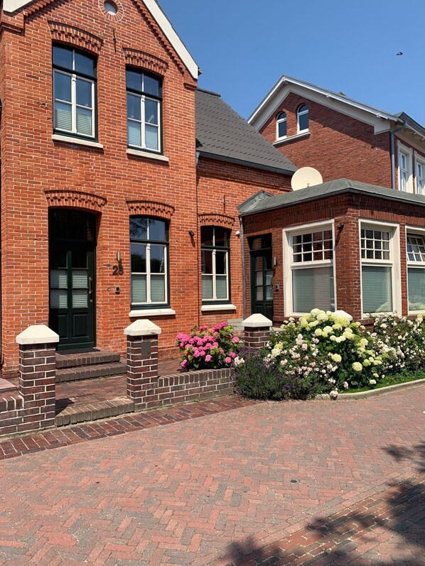 A brick building with a symmetrical facade, large windows, and a small garden with pink and white flowers.