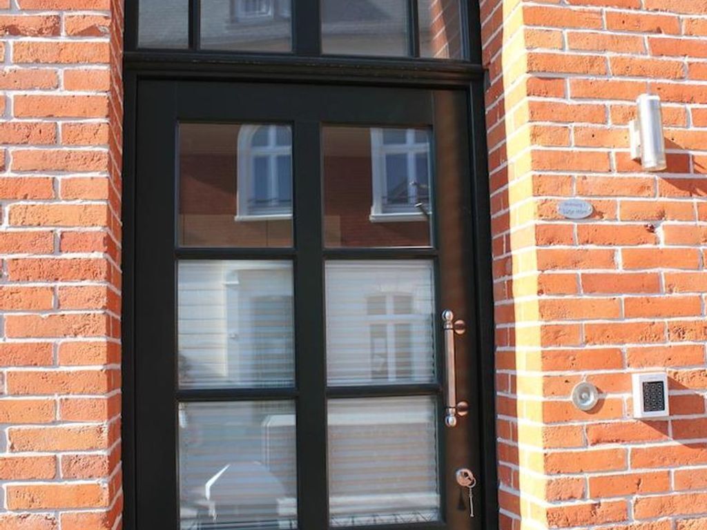 Una porta d'estructura negra amb una finestra, una clau i una cadeneta a una paret de maó.