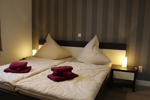 Un lit double avec deux oreillers et deux serviettes pliées, une table de chevet avec une lampe, et un mur à rayures verticales.