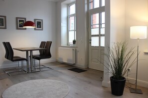 Een kamer met een eettafel, stoelen, een rode hanglamp, een plant in pot en een vloerlamp.