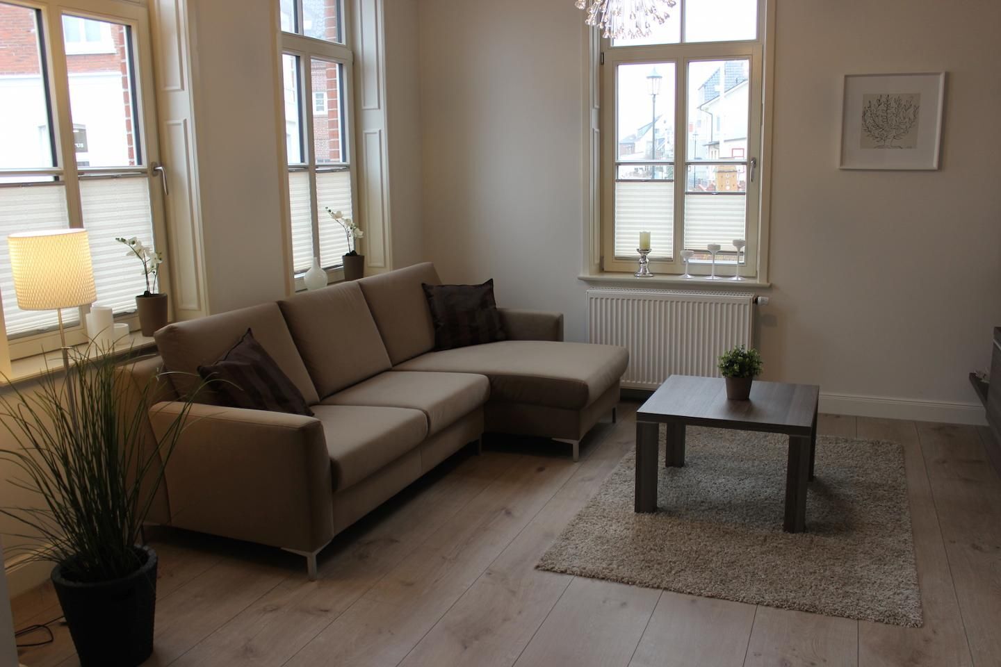 Un salon avec un canapé d’angle beige, une petite table, une plante en pot et un radiateur.