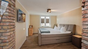 Quarto com cama, mesa de cabeceira, cômoda de madeira, parede de tijolos e janela com persianas.